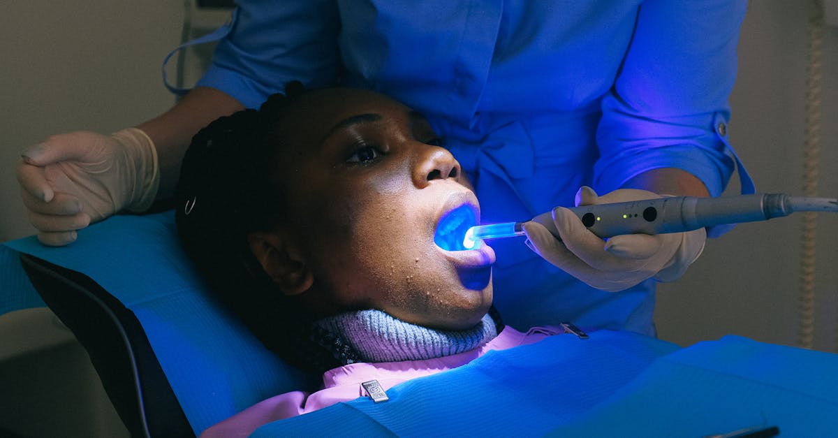 african american woman sitting in dental chair and receiving treatment with curing light from crop d